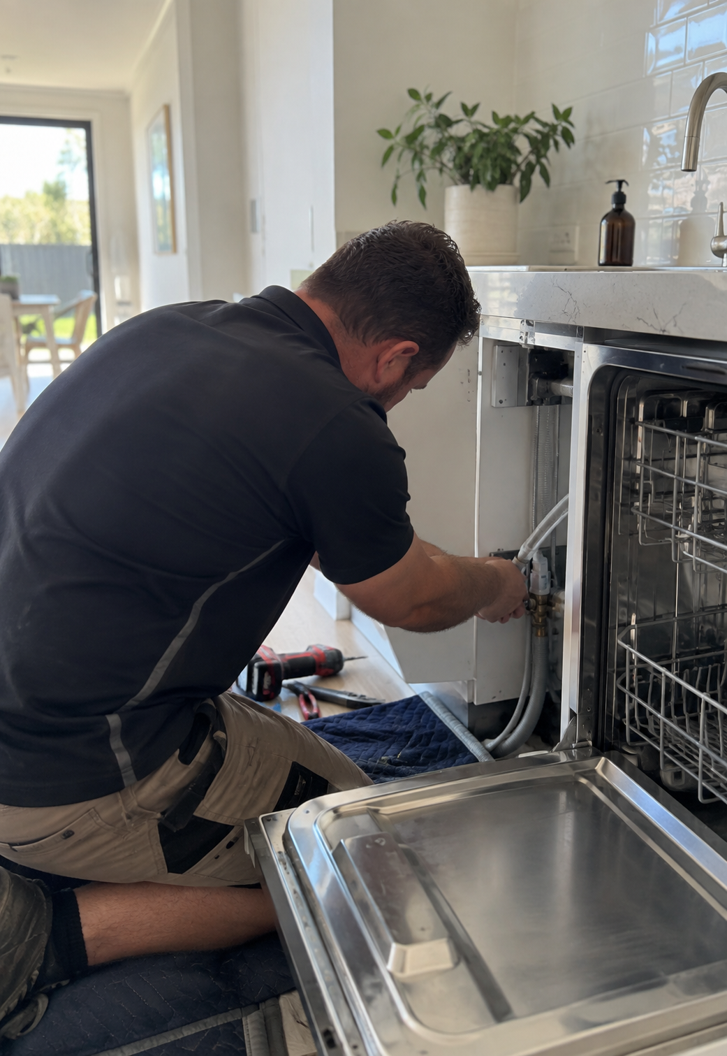 Plumber installing a dishwasher under a kitchen benchtop